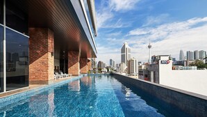 Un hotel moderno con piscina infinita en la azotea y vistas a un horizonte urbano.