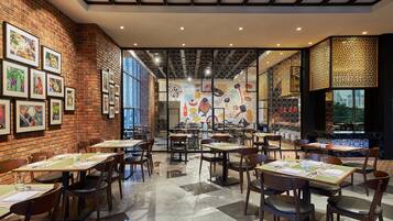 A restaurant with brick walls, framed pictures, and a tiled floor. Tables and chairs are set for dining.