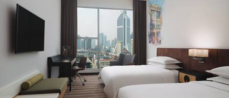 A hotel room with two beds, a desk, a chair, a television, and a large window with a city view.