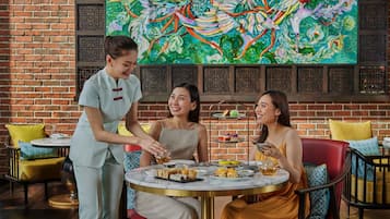 A restaurant with a brick wall and a colorful mural. There are three people seated at a table with various dishes and drinks.