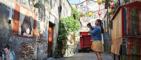 A narrow alleyway with old buildings, a mural, and hanging lanterns.