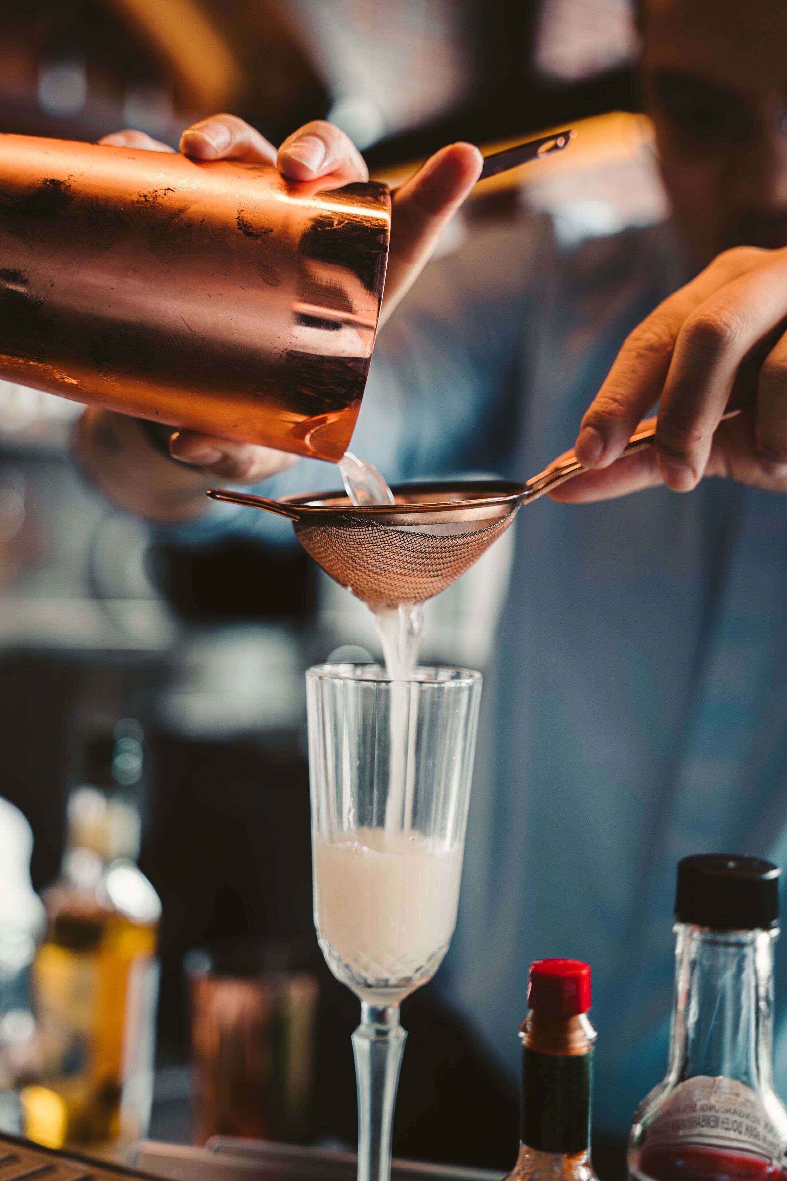 A bartender pouring a liquid into a glass using a strainer.