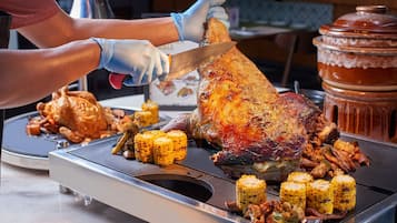 A person carving a large roasted turkey surrounded by vegetables and meats on a grill.