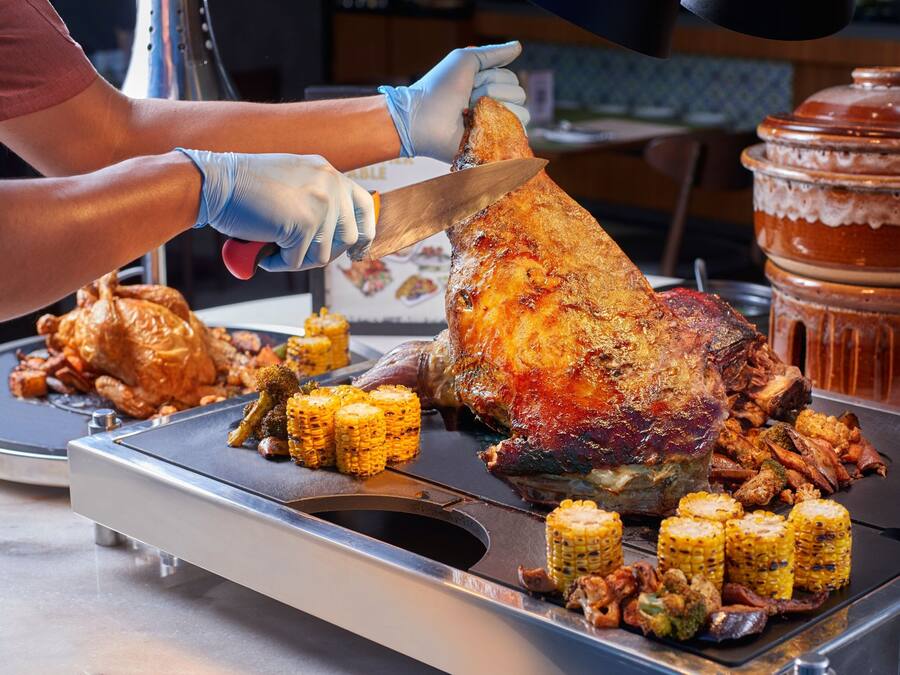 A person carving a large roasted turkey surrounded by vegetables and meats on a grill.