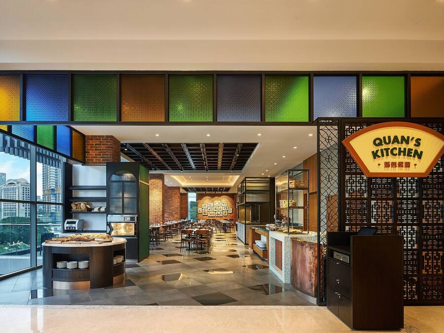 A modern restaurant with a central counter, multiple dining tables, and a view of the cityscape through large windows.