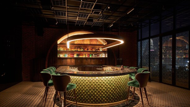 Una zona de bar con una barra curva, sillas tapizadas en verde y una pared con diseño.