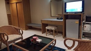 Quarto de hotel compacto com escrivaninha de madeira, televisão, frigorífico e mobiliário de vime.