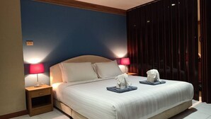 Et hotelværelse med en stor seng, to sengeborde, lamper og et vindue med mørke gardiner.