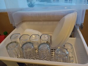 Ein Behälter aus Kunststoff mit weißem Deckel, der mehrere klare Glasflaschen und eine weiße Plastikschale enthält.
