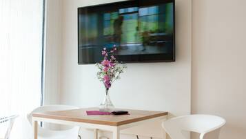A modern room with a wooden table, white chairs, a vase with flowers, and a mounted TV on the wall.