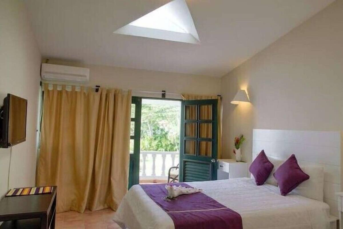 A bedroom with a bed, a desk, a chair, a window with curtains, and a ceiling fan.