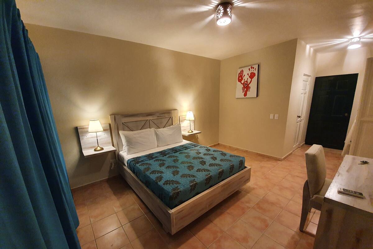 A bedroom with a bed, two bedside tables with lamps, a door, and a small table with a remote control.
