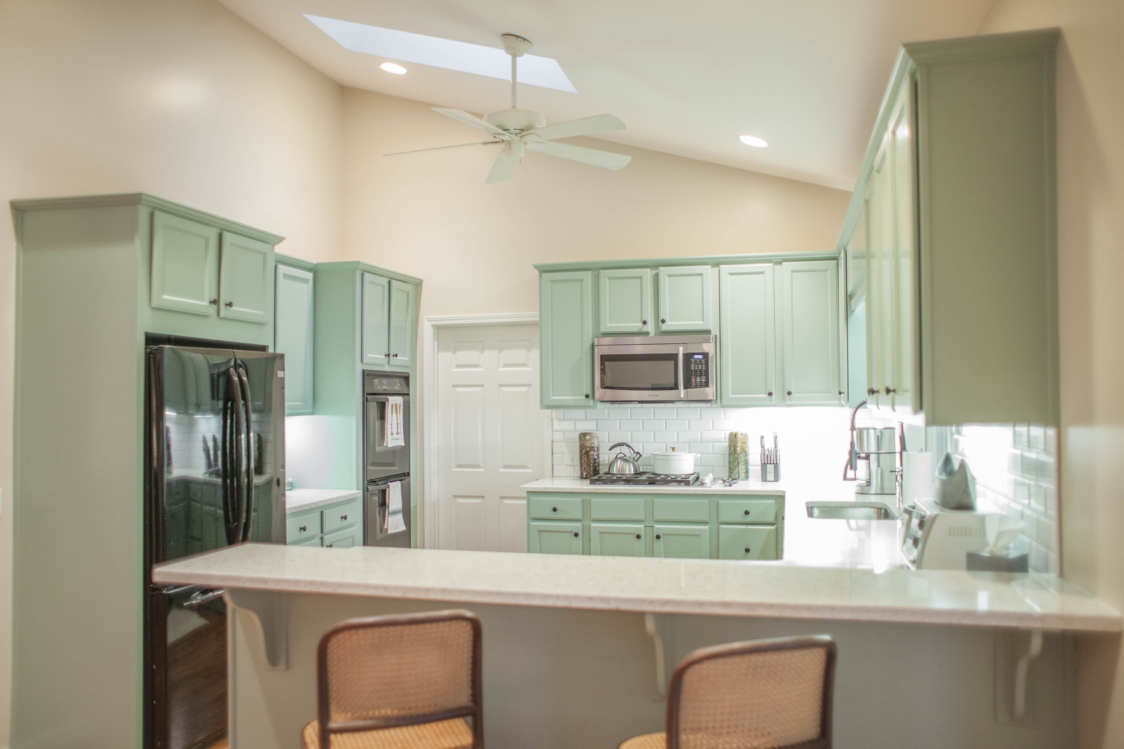 A kitchen with green cabinets, a microwave, a refrigerator, and a ceiling fan.