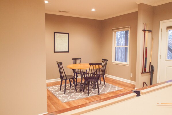 A dining area with a wooden table and chairs, a patterned rug, and a window with a view of trees.