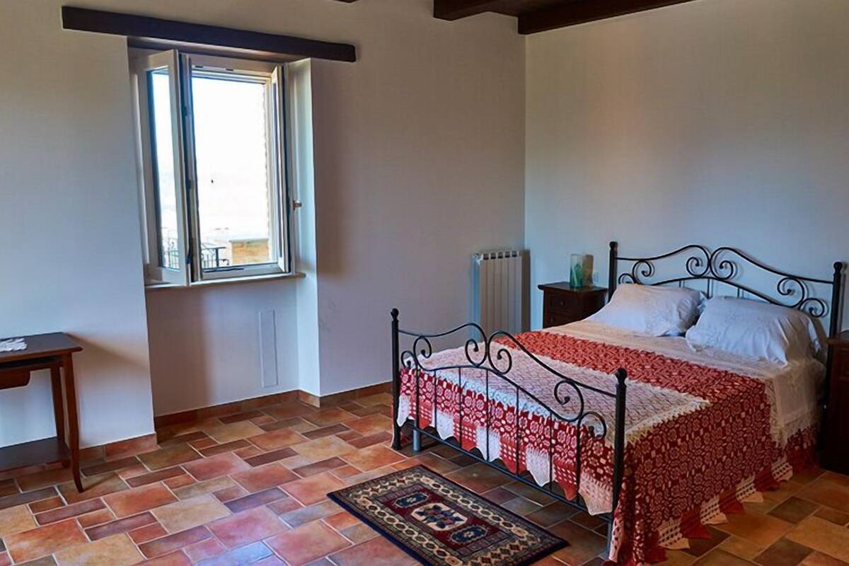 Une chambre à coucher avec un lit, une fenêtre, un radiateur, une table de chevet et une petite table.