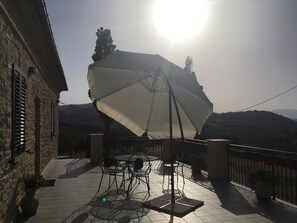 Un patio con una mesa y sillas, un paraguas grande y vistas a las colinas.