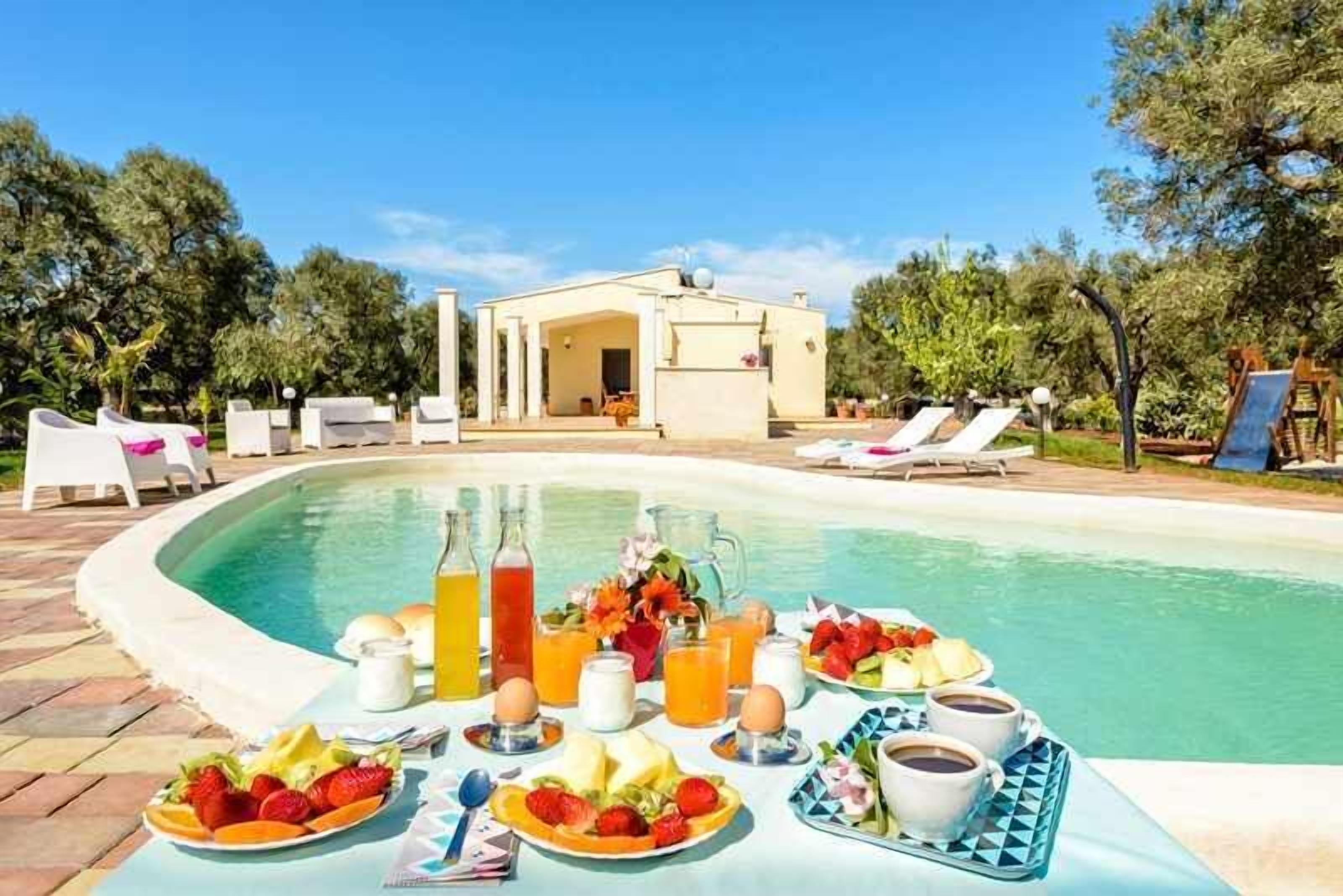 A poolside breakfast setup with a table, drinks, and fruit.