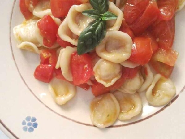 A plate of ravioli with tomatoes and a basil leaf.