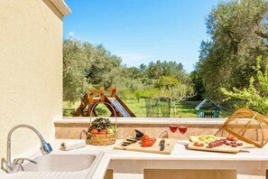 A balcony with a sink, a wooden table with food and drinks, and a view of a garden. - PRIVATE SWIMMING-POOL -Fenced- SEA close by- GAMES (San Vito Dei Normanni)