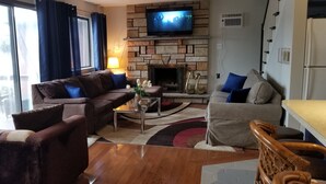 A living room with a stone fireplace, a television mounted above it, and a sofa set. - LAKEFRONT,Swim,enjoy&relax,7kayaks,SUP,paddlboat,firepit,PA,cabin,Fun,  (Tobyhanna)