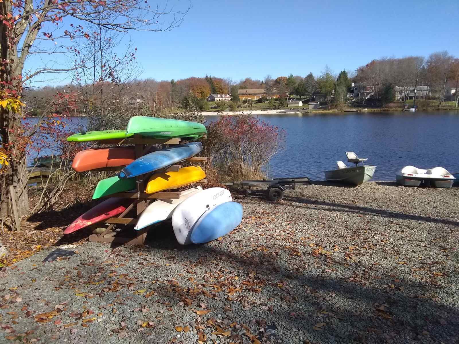 A gravel dock with kayaks and a small boat by a lake.