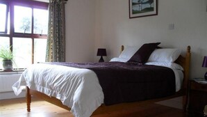 Une chambre avec un lit en bois, une fenêtre avec des rideaux, une table de chevet avec une lampe et un tableau encadré au mur.