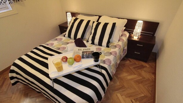 A neatly made bed with striped bedding, a tray with fruits and a drink, and a book titled "EL PAIS" on a bedside table. - Elegance Plaza Mayor with Balcony (Madrid)