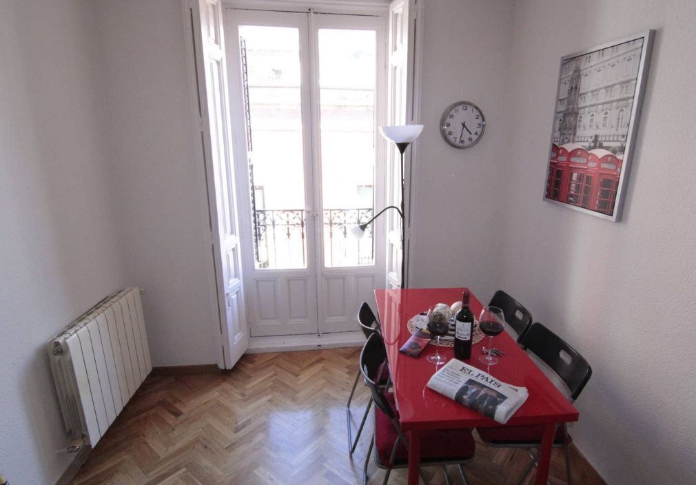 A dining area with a red table, chairs, a clock, and a radiator. - Elegance Plaza Mayor with Balcony (Madrid)