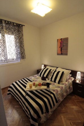 A neatly made bed with striped bedding, a bedside table with a lamp, and a window with patterned curtains. - Elegance Plaza Mayor with Balcony (Madrid)