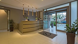 A modern reception area with a curved desk, pendant lighting, and a large glass door leading outside. - Icarus Suite Apartments (Rethymno)