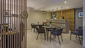 A modern dining area with round tables and wicker chairs, a reception desk, and a wooden partition. - Icarus Suite Apartments (Rethymno)