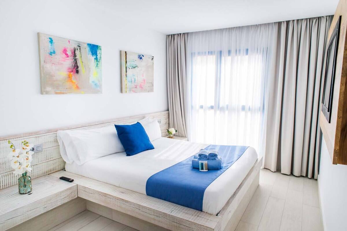 Une chambre d’hôtel avec un lit, une table de chevet, un vase de fleurs et deux tableaux abstraits accrochés au mur.