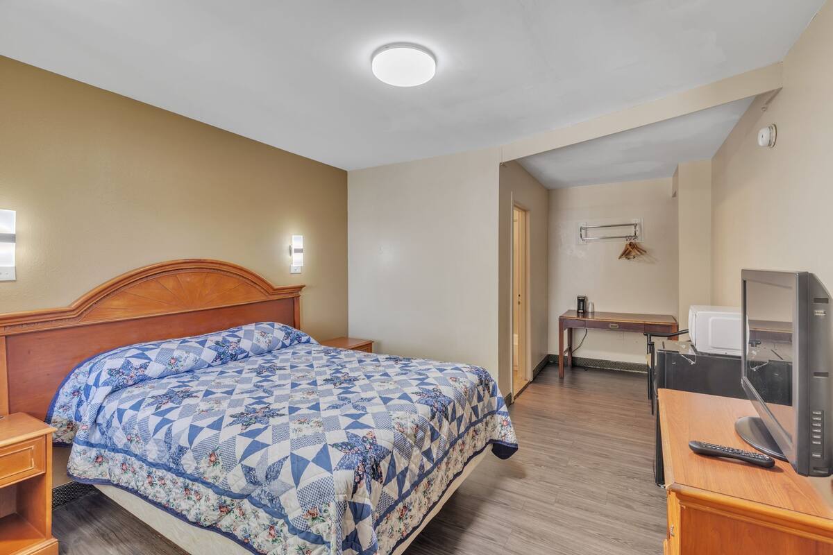 A bedroom with a bed, bedside table, TV, and a desk with a chair.