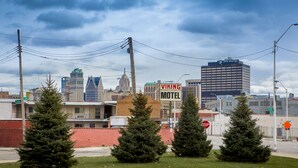 A motel with a signboard, surrounded by trees and a cityscape in the background. - Viking Motel (Detroit)