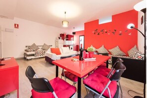 A modern living room with a red dining table, two sofas with patterned cushions, and a red wall with bird decals.