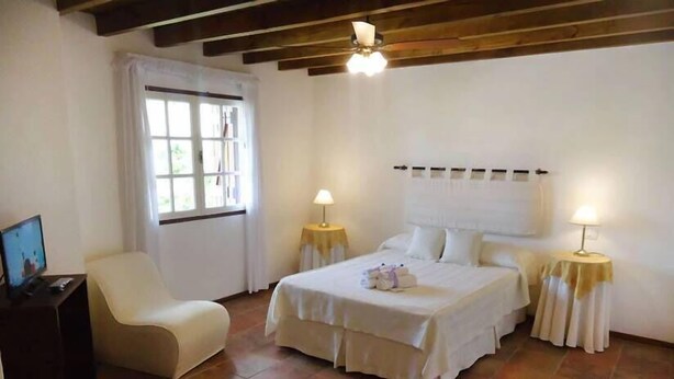 A bedroom with a bed, two bedside tables with lamps, a chair, and a television on a stand. - Hosteria Sajonia (Villa Gesell)