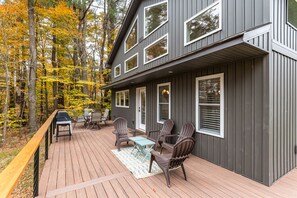A modern house with a deck, outdoor furniture, and a view of autumn trees. - Modern Berkshires Cottage  🌲 Gas Stove, Large Deck & W/D + 7 mins to Otis Ridge (East Otis)