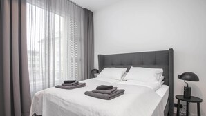A modern hotel room with a large bed, grey curtains, and a bedside table with a lamp.