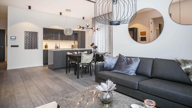 A modern living room with a dark sofa, a coffee table with decorative items, and a dining area with a chandelier.