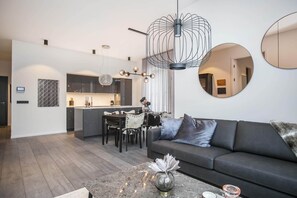 Una sala de estar moderna con un sofá oscuro, una mesa de centro con adornos y una zona de comedor con candelabro.