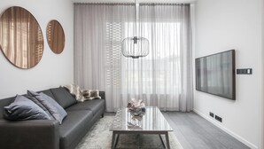 A modern living room with a dark grey sofa, a glass coffee table, and a large TV on the wall.