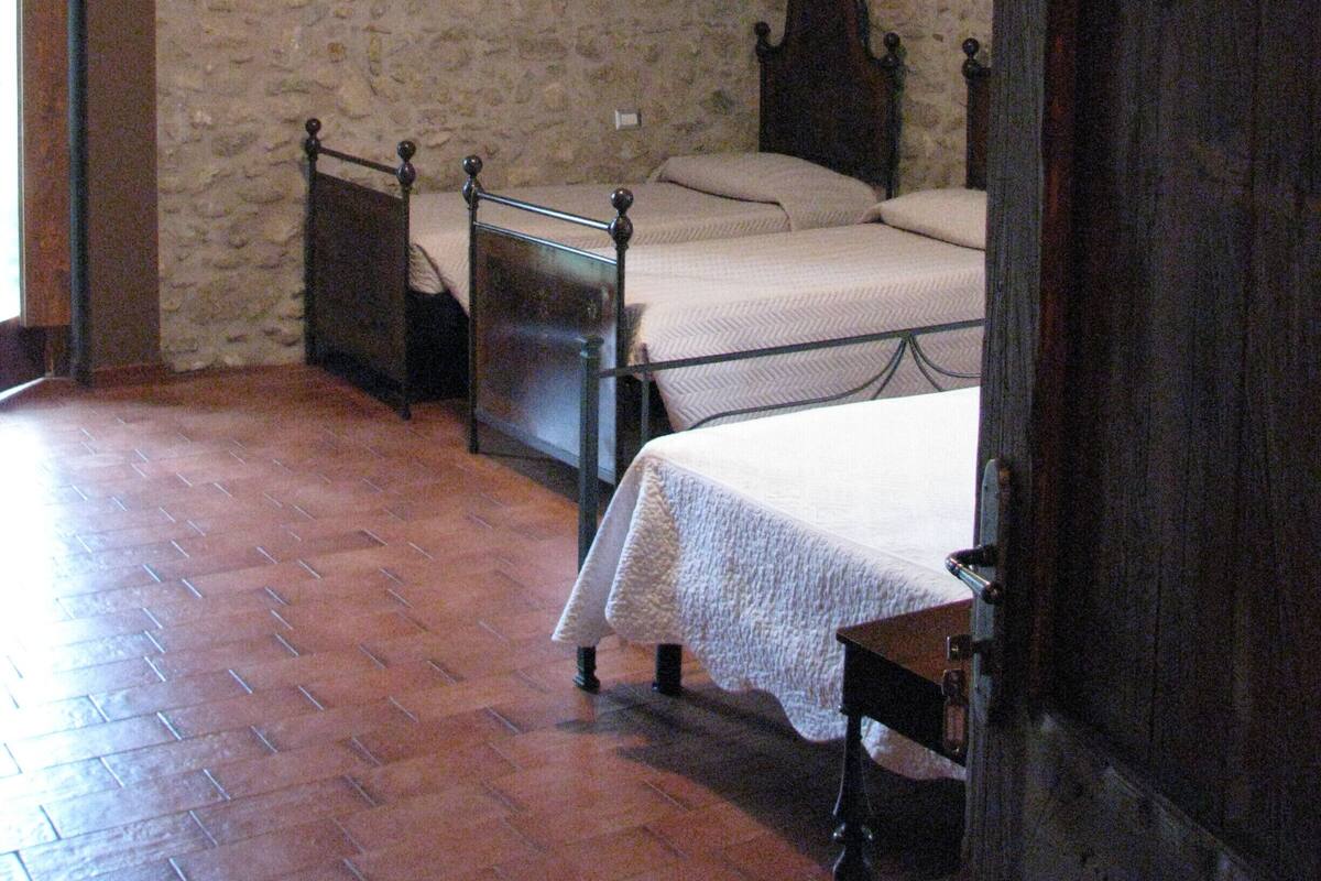 Une chambre avec deux lits, des murs en pierre, un tableau représentant des arbres et une porte en bois.