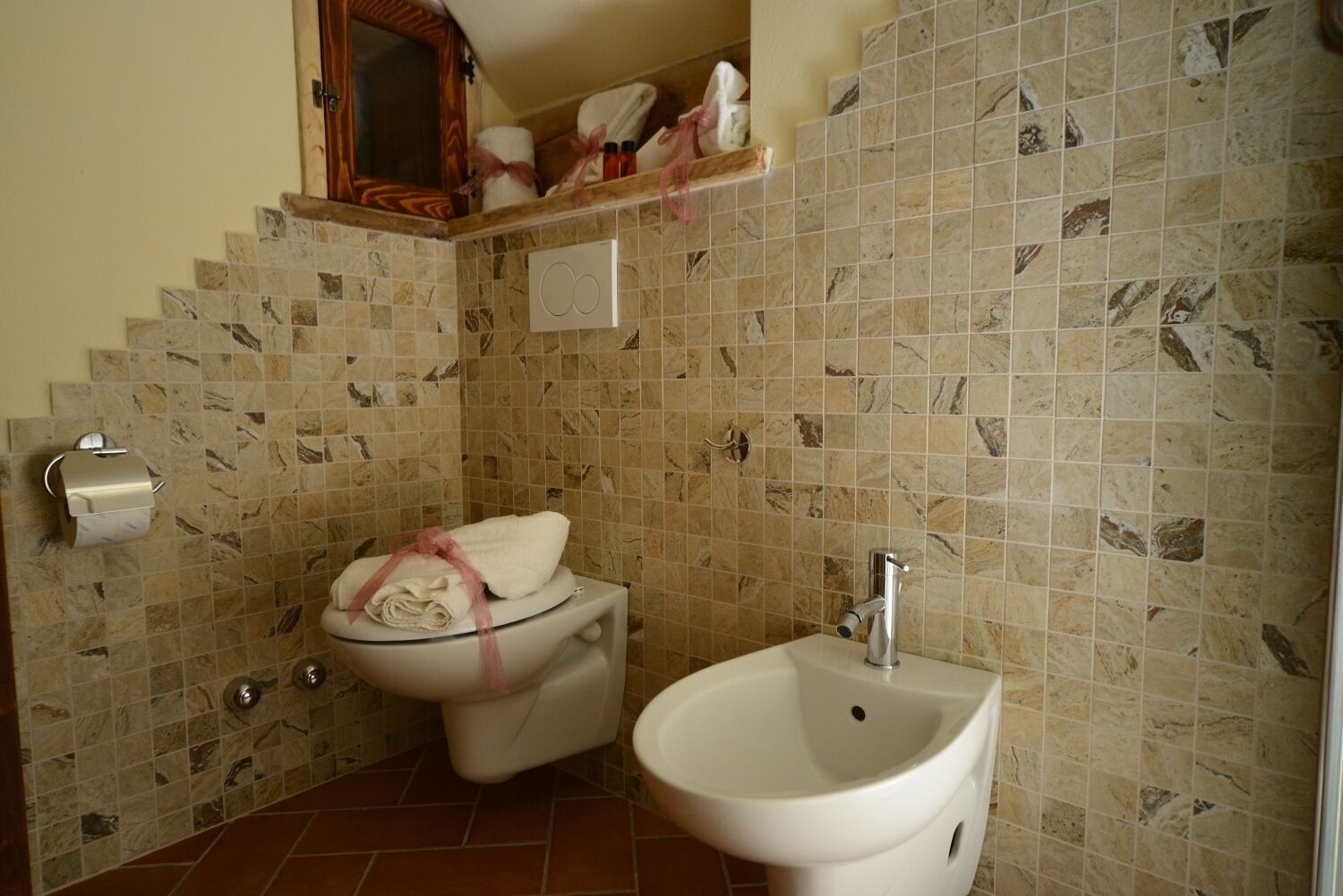 A bathroom with a toilet, bidet, and sink, all with marble tile backsplashes.