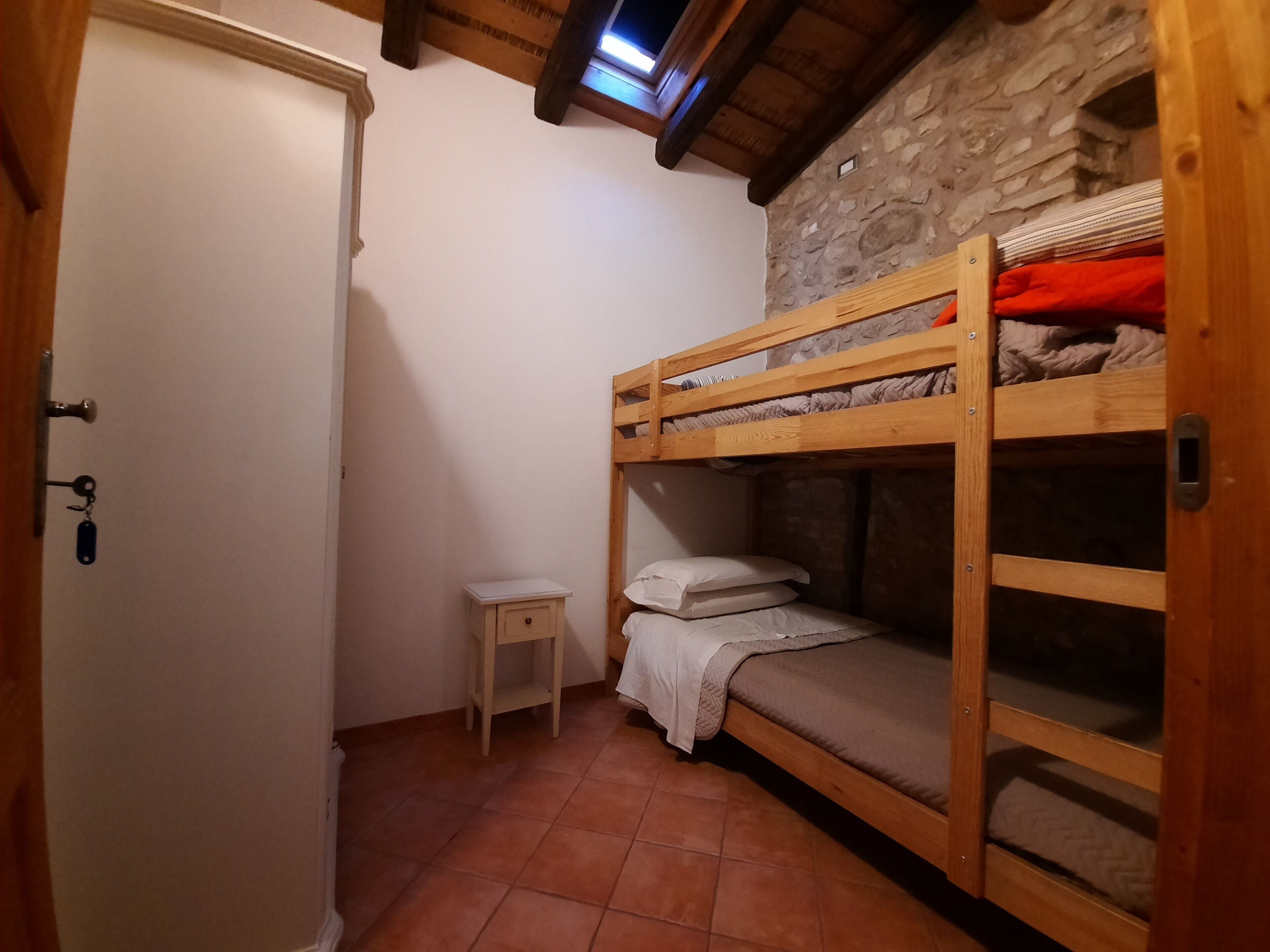 A small, cozy room with a bunk bed, a small bedside table, and a stone wall.