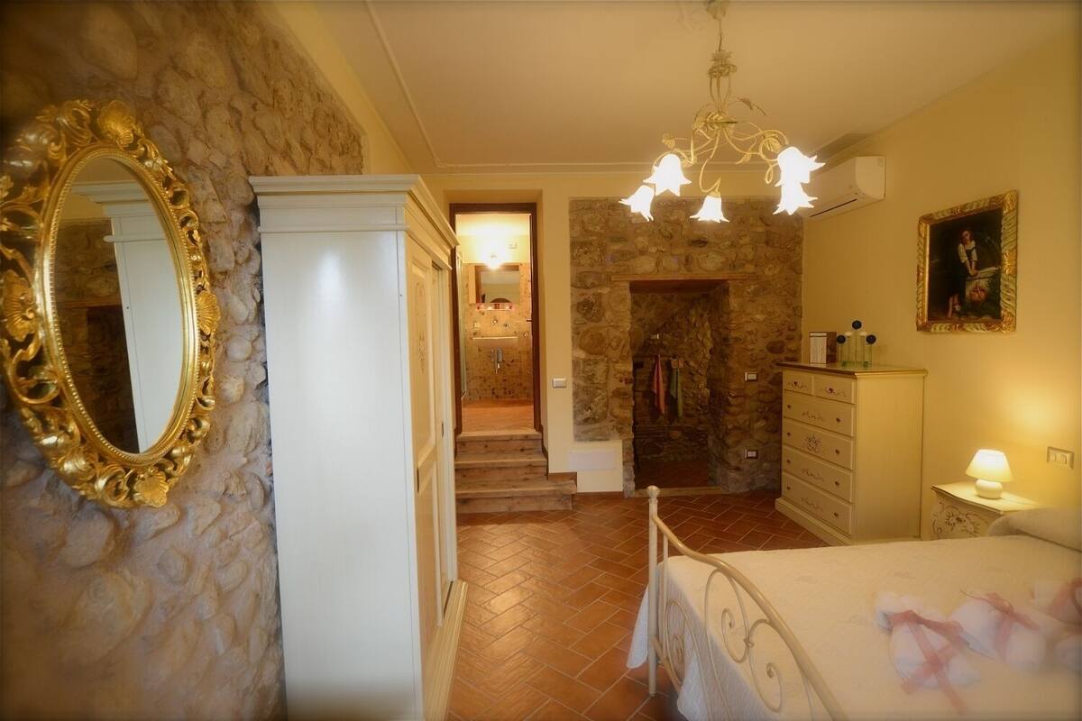 Une chambre à coucher avec un lit, une commode et un miroir. Un escalier mène à une salle de bain équipée d’une douche et d’un lavabo.