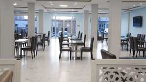 Een ruime eethoek met meerdere tafels en stoelen, grote ramen en een modern plafondontwerp.