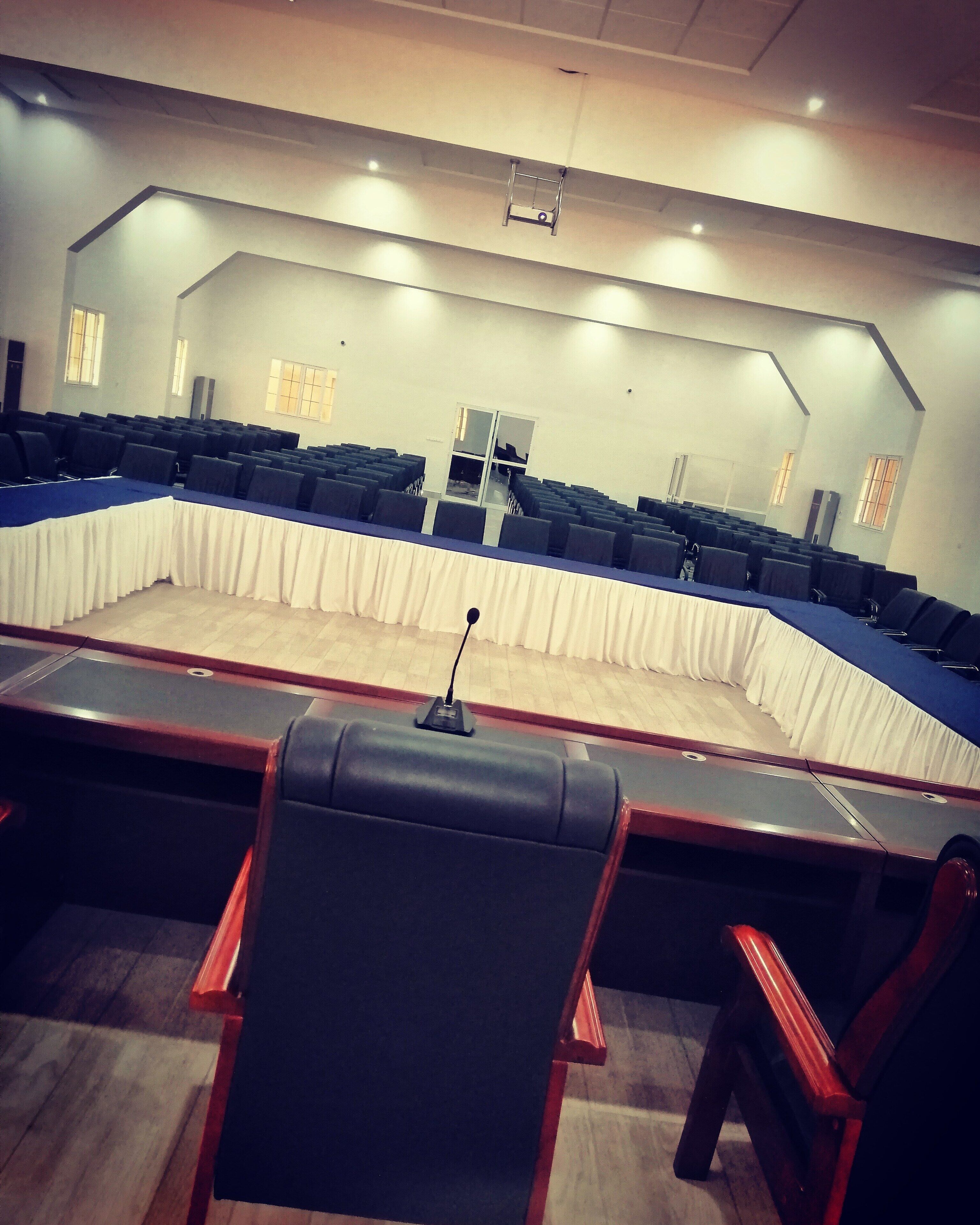 Un salón de conferencias con filas de sillas, un atril y una gran mesa.
