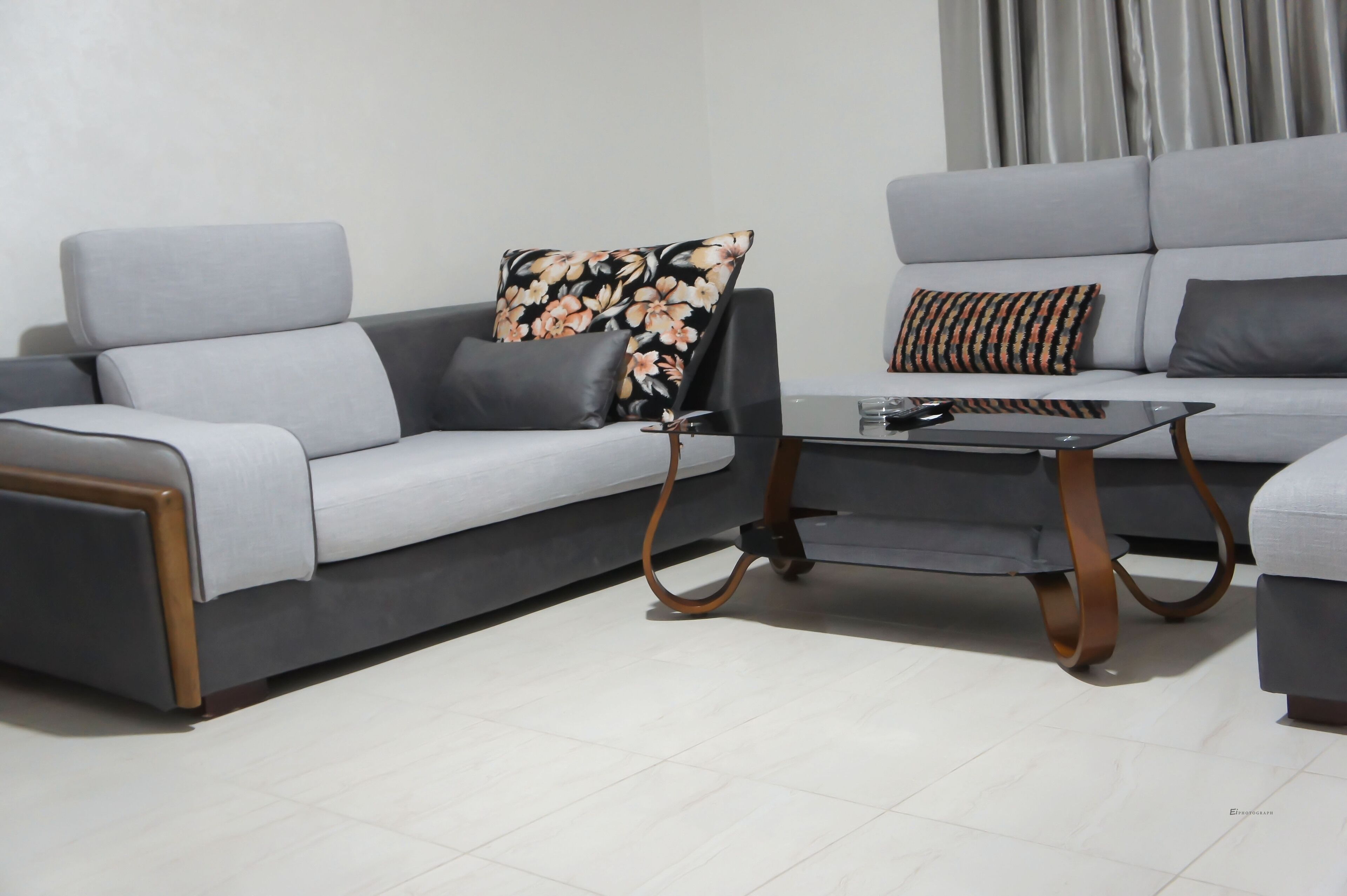 A modern living room with a grey sofa, a black coffee table, and a floral pillow.