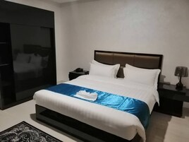 Habitación de hotel moderna con una cama grande, una mesita de noche, una lámpara y vistas de la ciudad a través de un ventanal amplio.