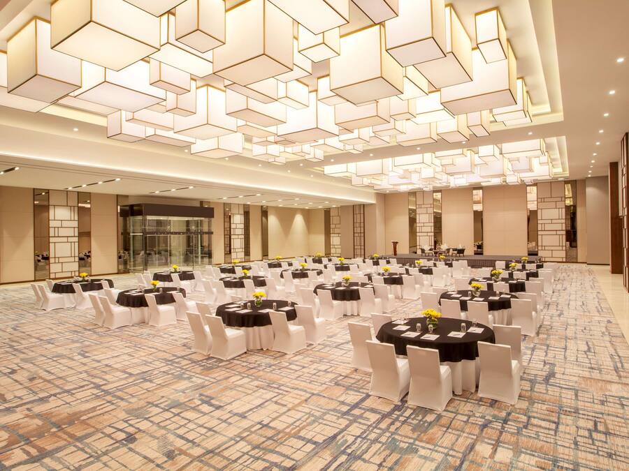 Una amplia sala de conferencias con varias mesas redondas, sillas blancas y una alfombra estampada.